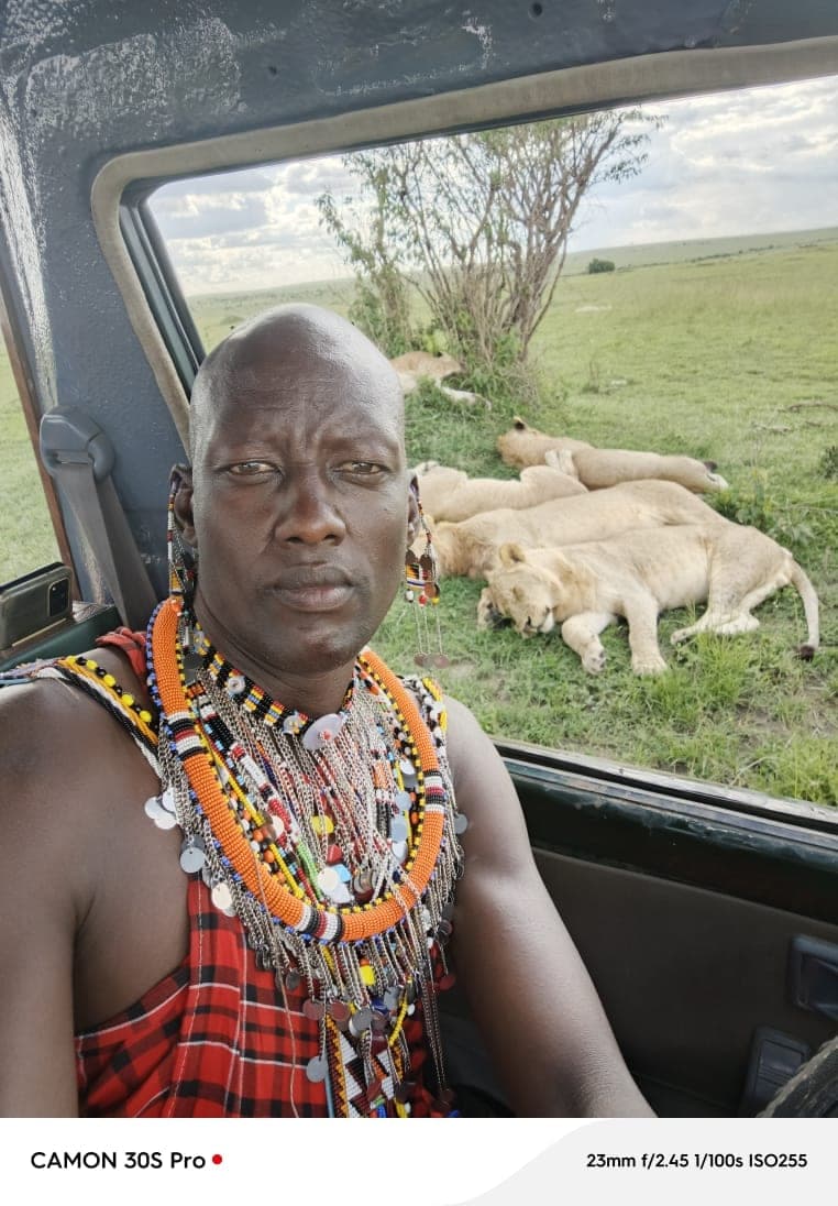 Jackson Karia, your Maasai guide, on a safari vehicle with lions resting behind him